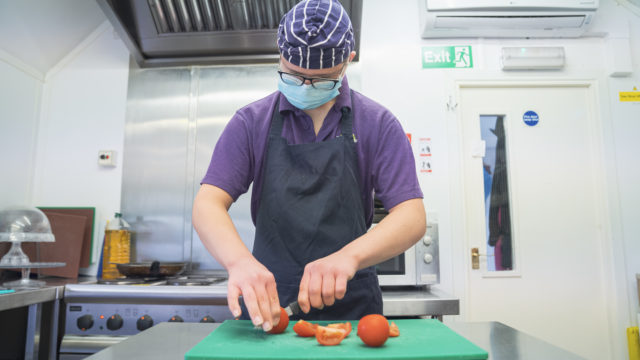 Student chopping tomatoes in commercial kitchen