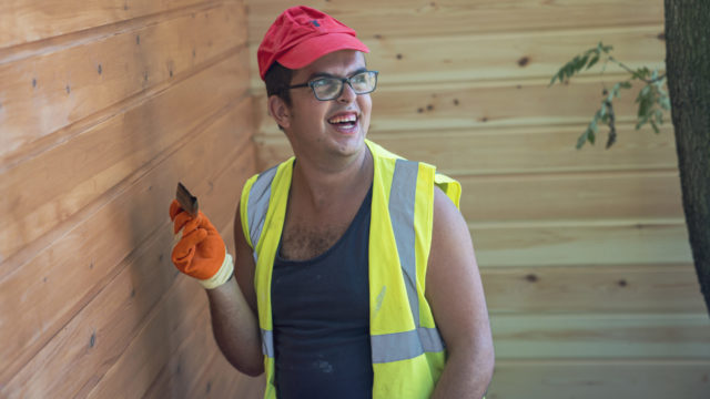 Student smiling whilst painting wooden building