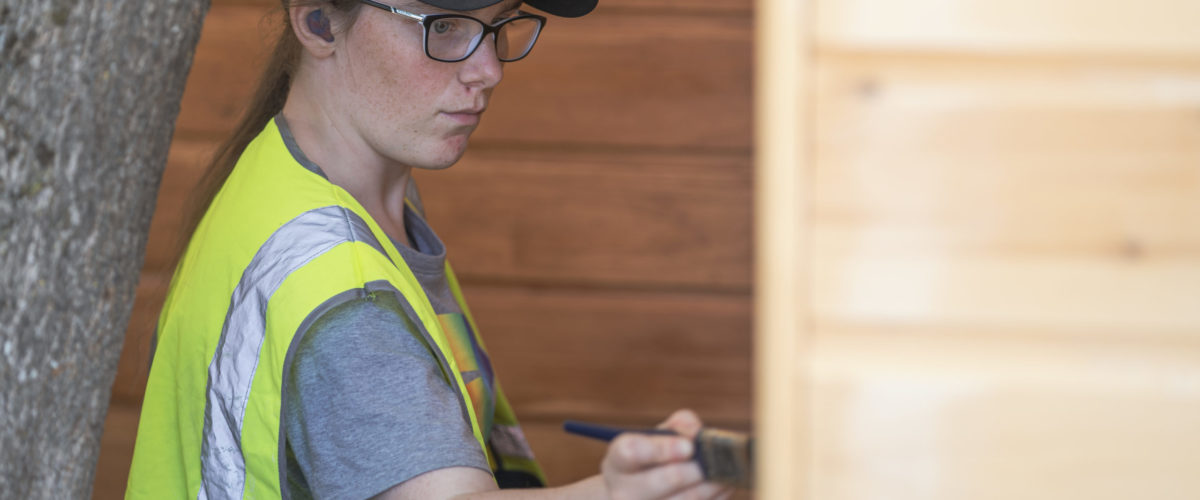 Student working outside painting wooden building