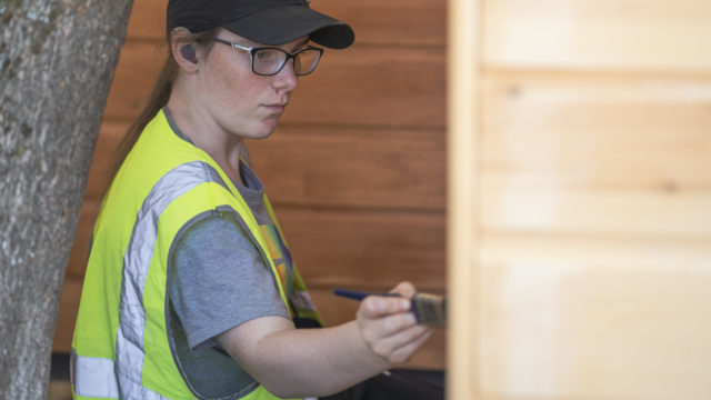 Student working outside painting wooden building