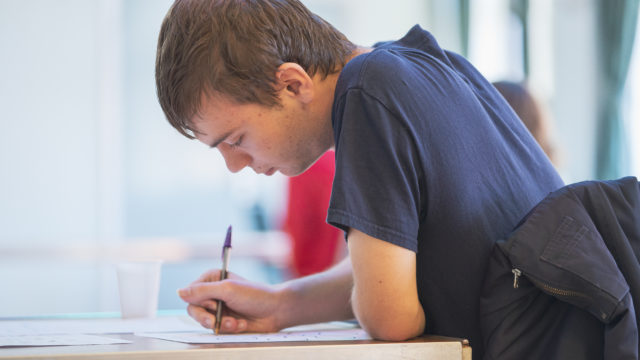 Student at desk holding pen concentrating on worksheet