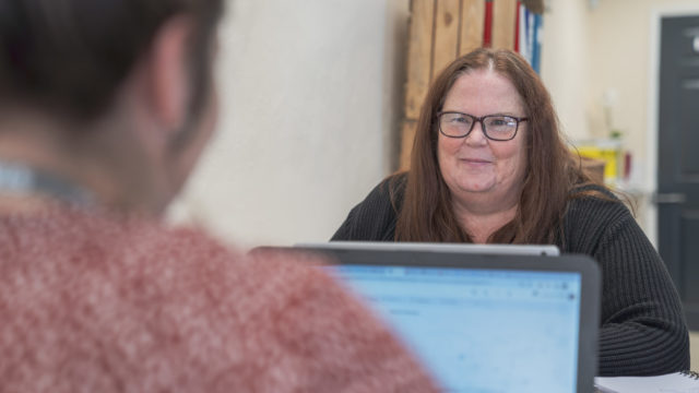 Staff member smiling across the laptop at another person