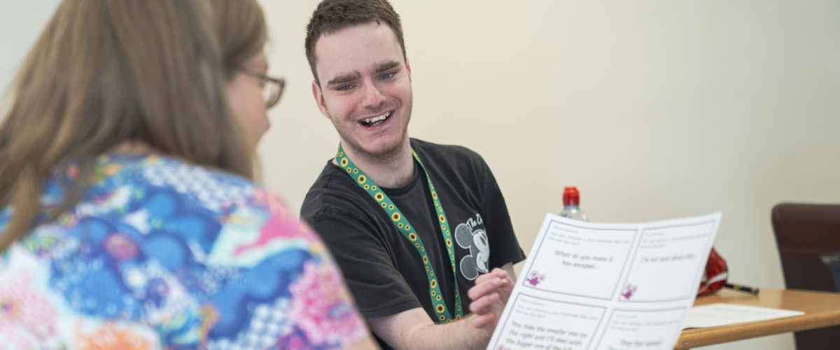 Student smiling whilst showing a document to a staff member