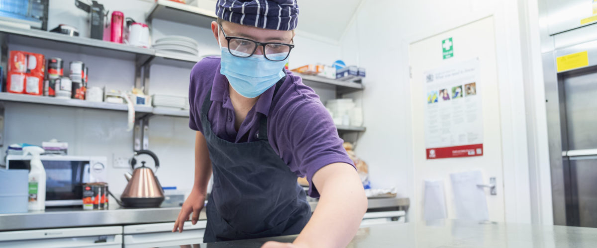 Student wiping down industrial kitchen