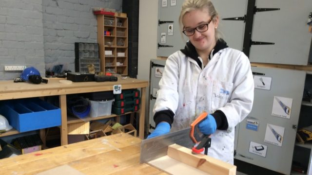 Student using saw on wooden block in woodwork