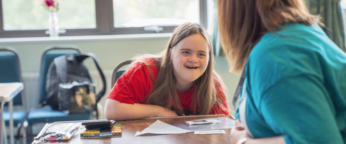 Student grinning whilst talking to a Learning Support Assistant