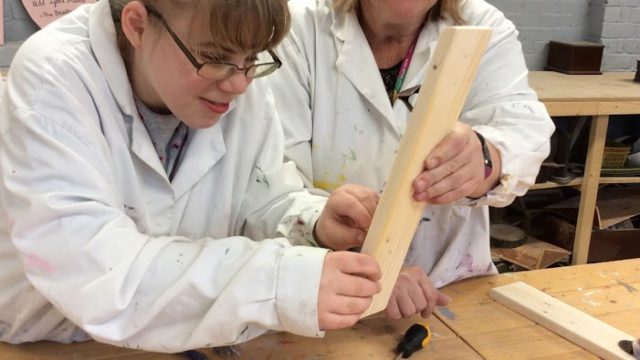 Day Service member working on a piece of wood with help from a staff member