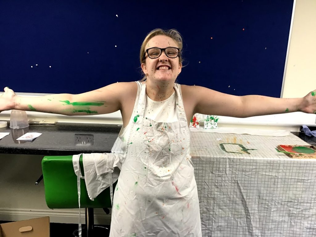 Student smiling with arms out covered in paint splashes