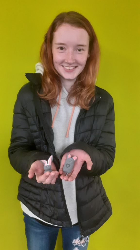 Student smiling holding a clay rabbit and mouse