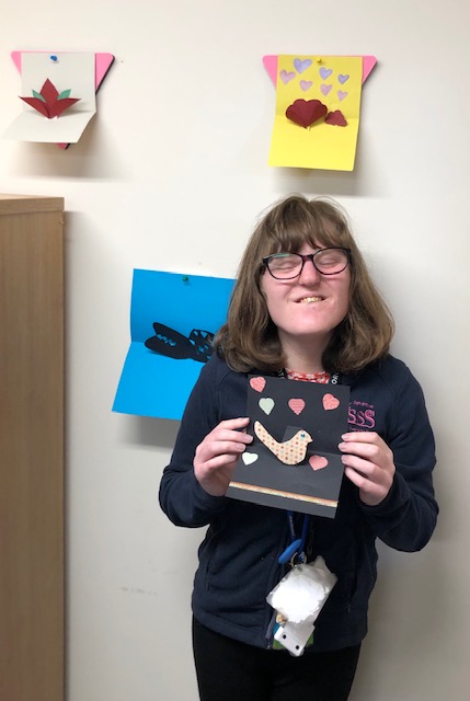 Student smiling holding their pop out card of a bird
