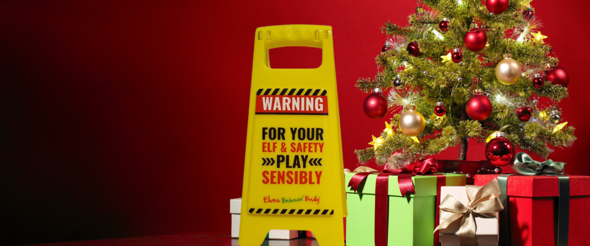 Sign saying WARNING, for your elf & safety play responsibly in front of a Christmas tree