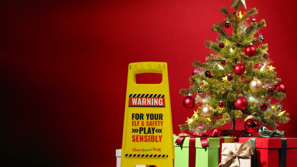 Sign saying WARNING, for your elf & safety play responsibly in front of a Christmas tree