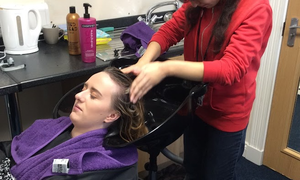 Student washing staff member's hair in salon sink