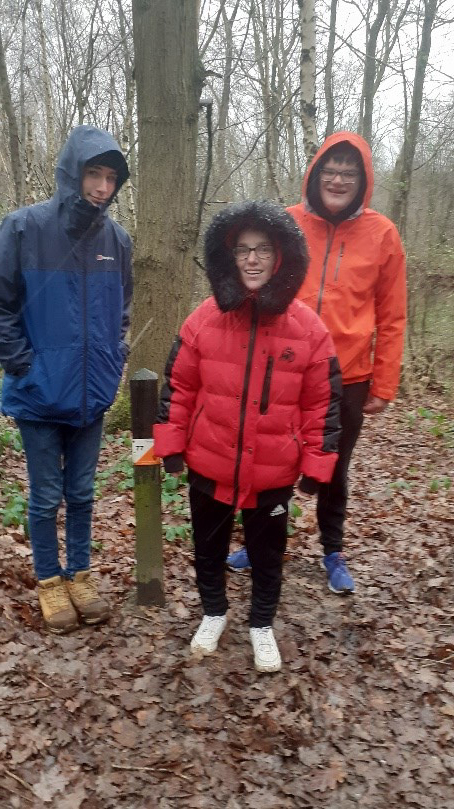 Students smiling whilst pointing at an orienteering marker in the outwoods
