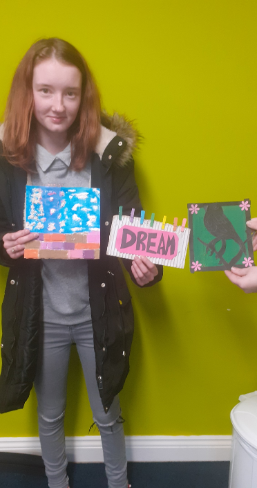Student holding three pieces of mixed media artwork