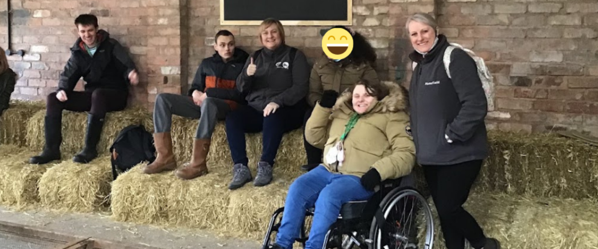 Students and staff smiling at the camera whilst sat on hay bales at the farm