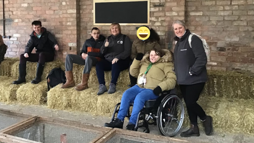 Students and staff smiling at the camera whilst sat on hay bales at the farm