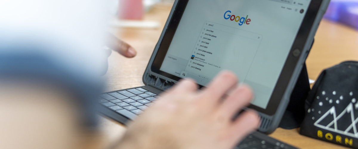 Hands typing on a keyboard attached to an ipad that has google on the screen