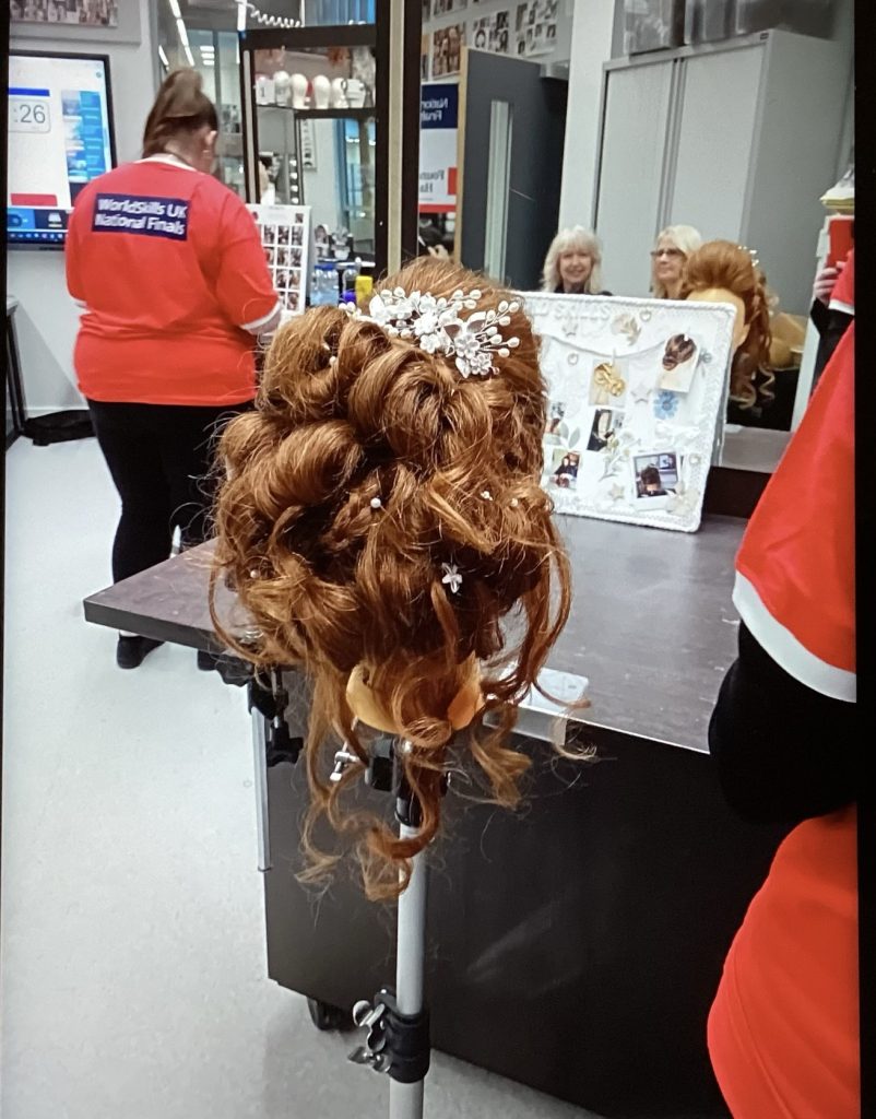 Skye's final hairstyling look for the competition: a bridal updo with plaits, twists, and white elegant and floral accessories.