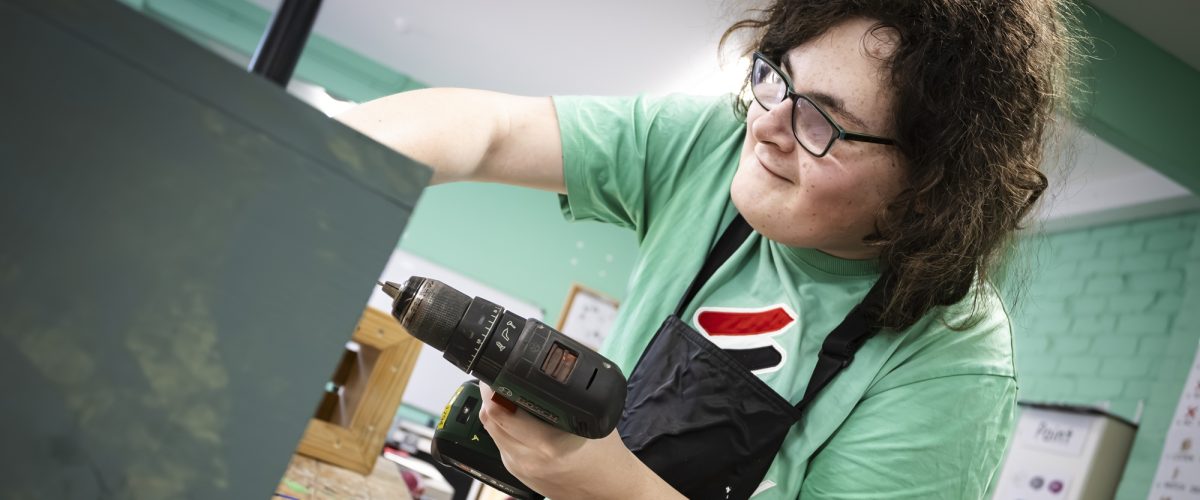 Student using drill on a wooden box in woodwork