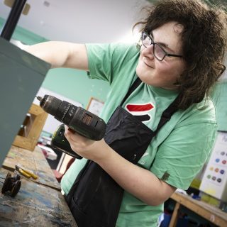 Student using drill on a wooden box in woodwork