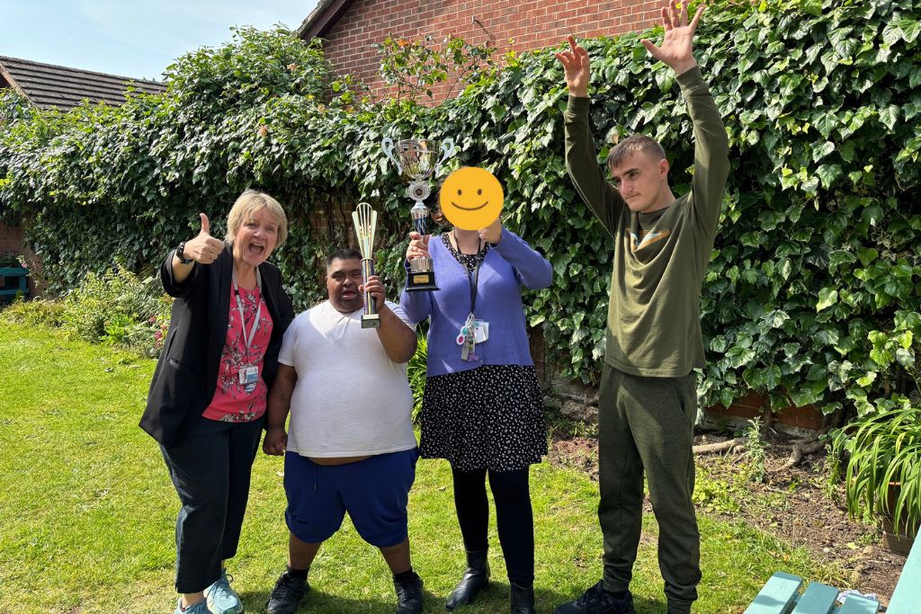 Image of Homefield principal Tracey Forman, alongside 3 students, all celebrating and holding two trophies.