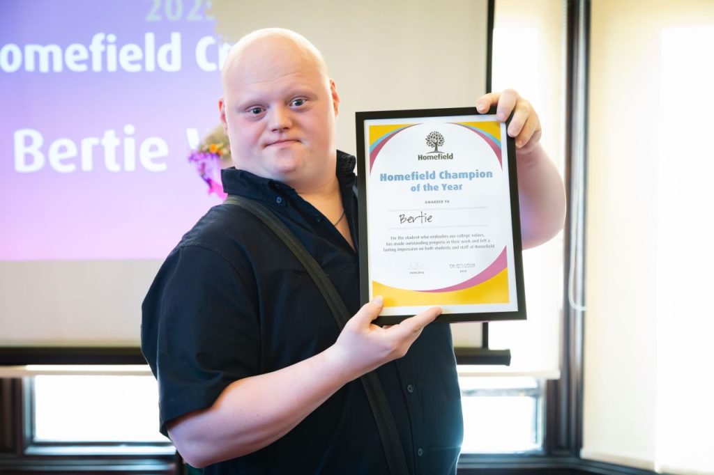 Pathway 2 graduate Bertie smiling at the camera while holding up his "Homefield Champion of the Year" award certificate