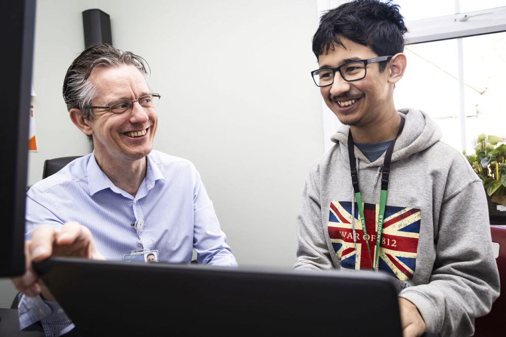 Pathway 3 student Dan and Homefield's IT Manager Paul smiling while working together in front of a laptop during Dan's IT work placement.