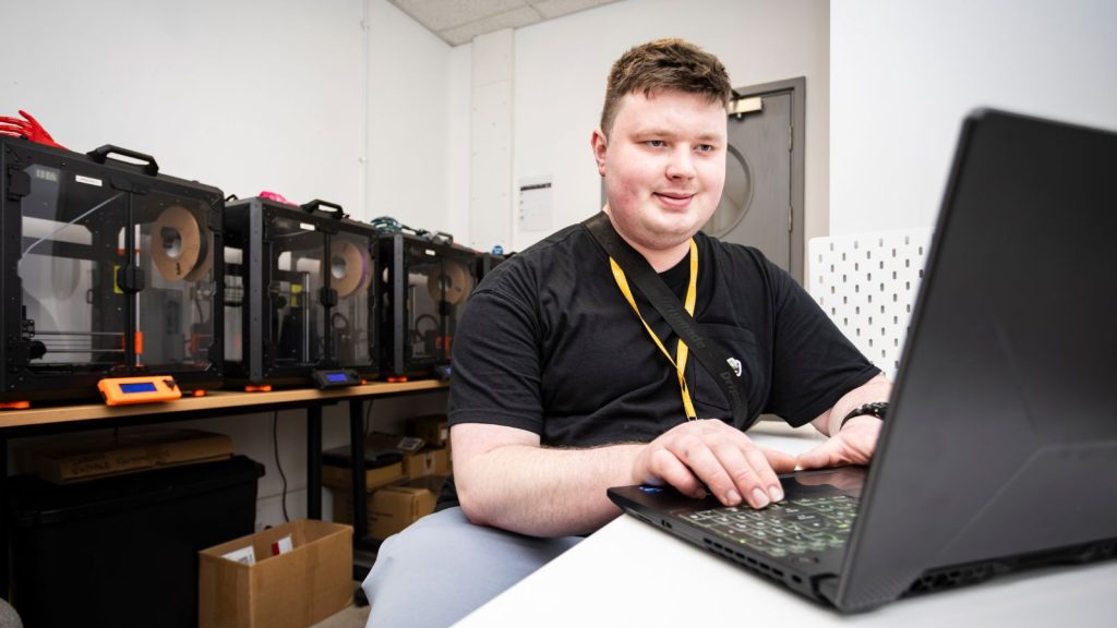 Henry W sitting at his desk, working on his laptop and smiling.