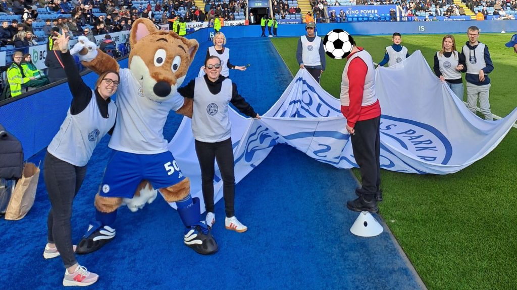 A picture of some of our staff and students posing cheerfully for the camera alongside the Leicester City fox mascot.