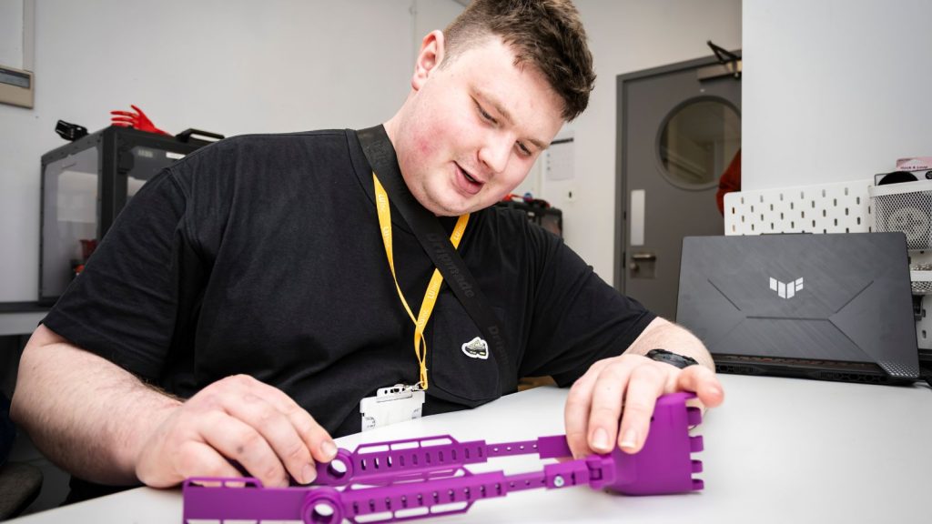 Henry sitting at his desk, working on a purple 3D-printed prosthetic hand