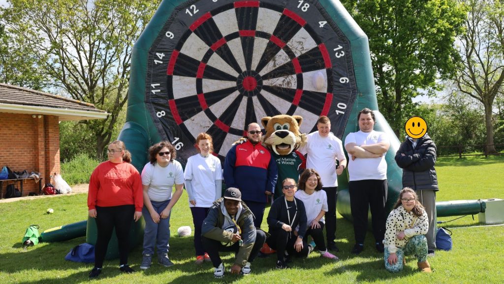 A group photo of the rugby team posing in front of the inflatable dartboard with Welford the Tiger.