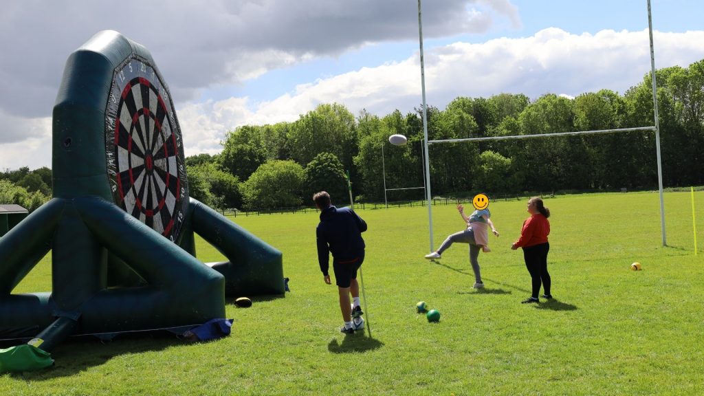 A photo of some of the attending students trying to kick the rugby ball onto the inflatable dart board.