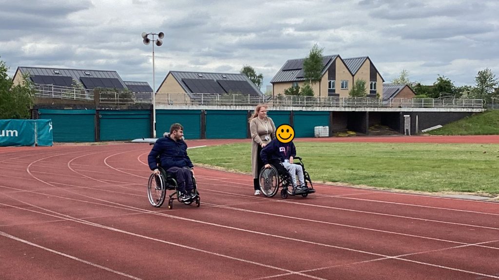 two of our students in wheelchairs on the race track, one of them being supported by a staff member