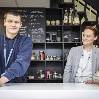 Student and staff member behind the serving bar at a coffee shop