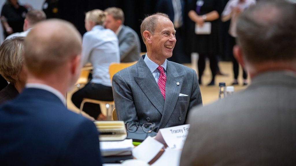 A photo of His Royal Highness, the Duke of Edinburgh, smiling at a table surrounded by other event attendees