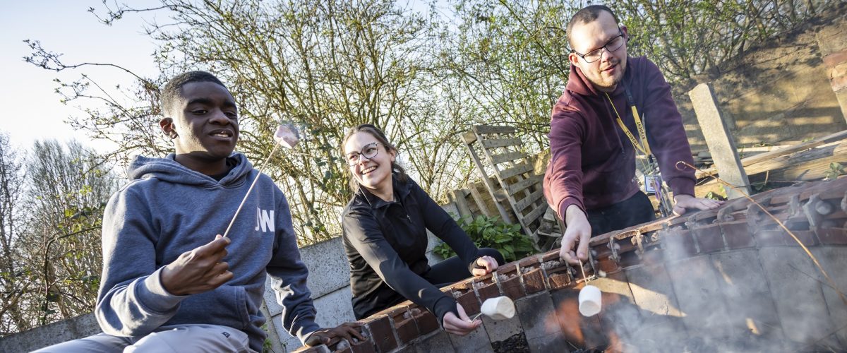 Two students and one staff roasting marshmallows